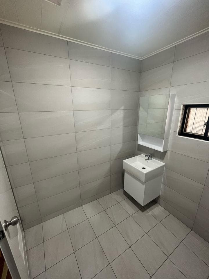 1) 這是一張浴室的照片,牆壁和地板都鋪著白色瓷磚,右上角有一個鏡子和洗手台