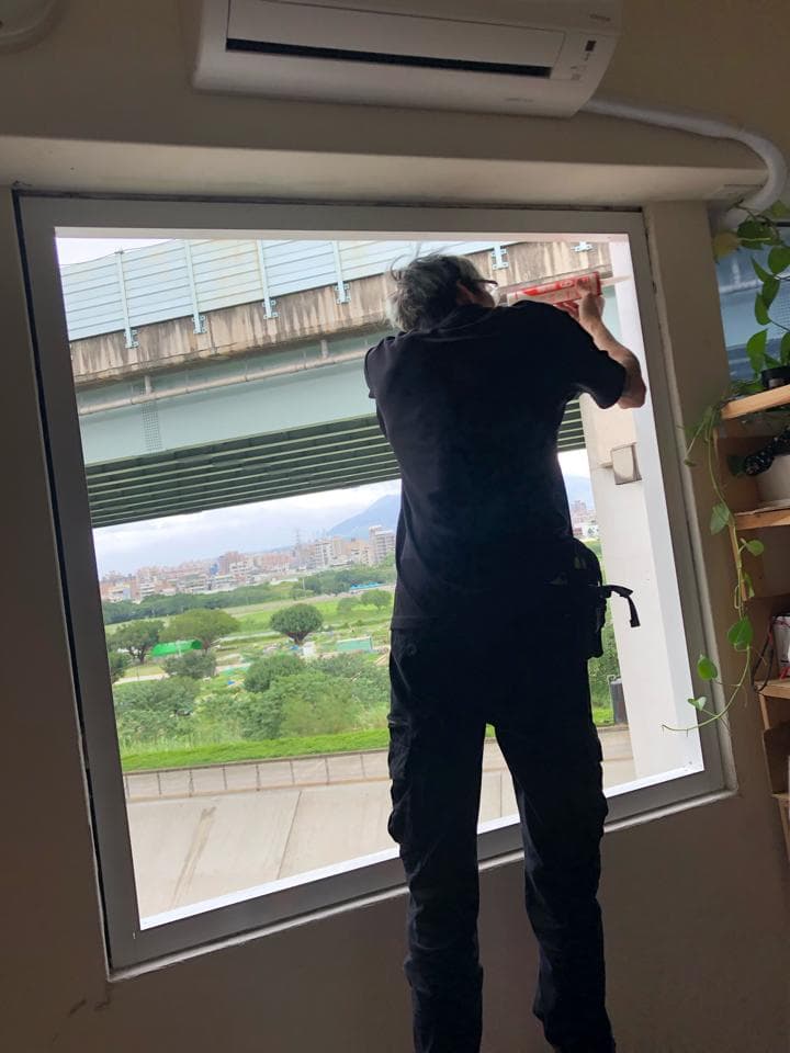 1) 照片中有一位身穿黑色衣服的男性站在窗户旁,面向窗外,窗户可以看到城市景色