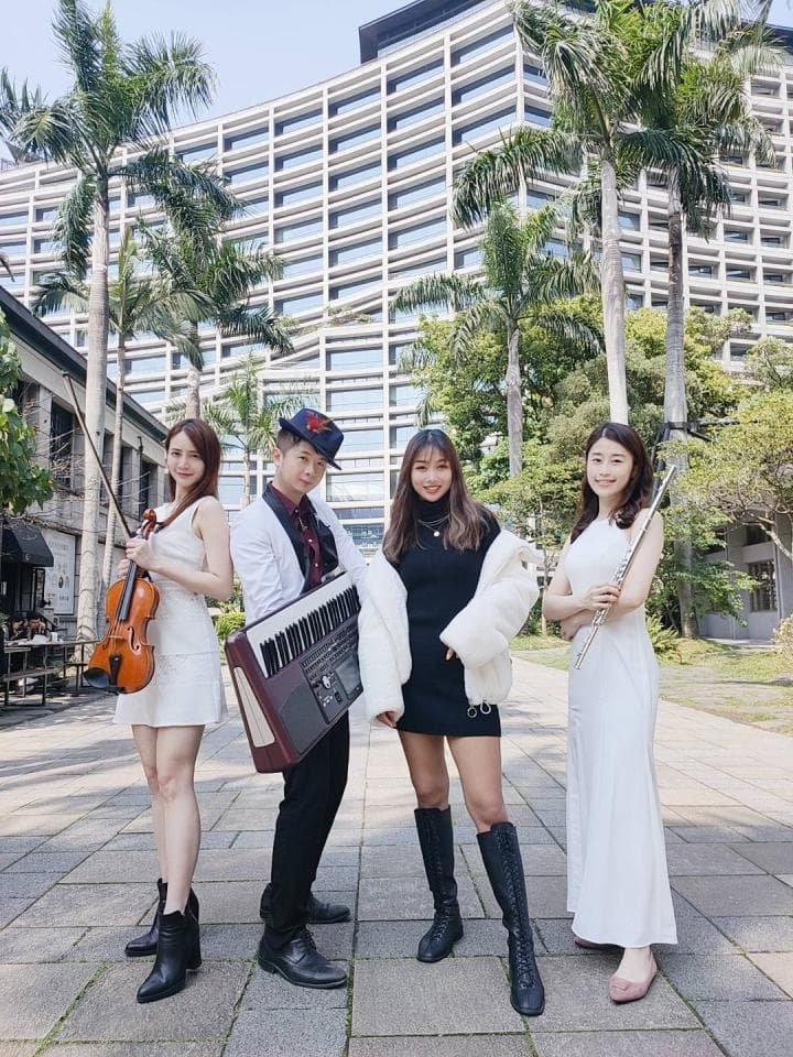 這張照片是四個年輕人站在現代建築物前,他們演奏著不同的樂器,看起來很開心。