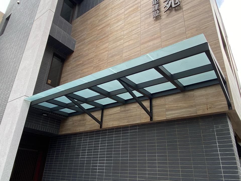 這張照片是一棟建築物的外觀,有一個玻璃屋頂,屋頂由黑色的金屬支撐架支撐,牆面以木紋磚和黑色磚塊裝飾。