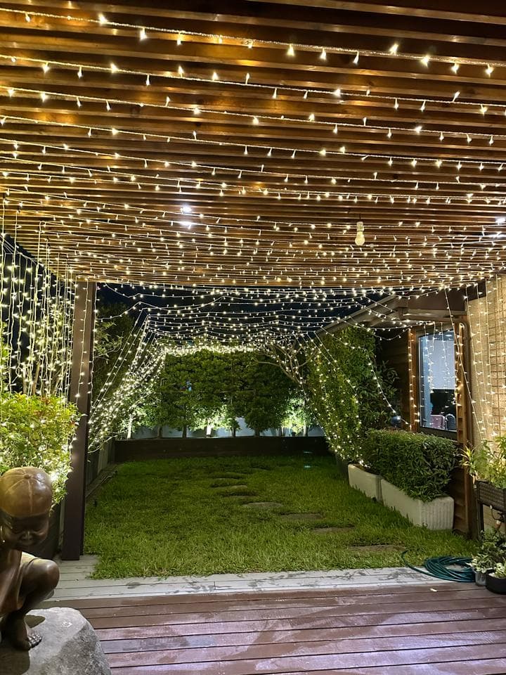 這張「戶外燈光裝飾」的照片是,一個被燈光裝飾的戶外空間,有木製的棚架和綠色的草坪。