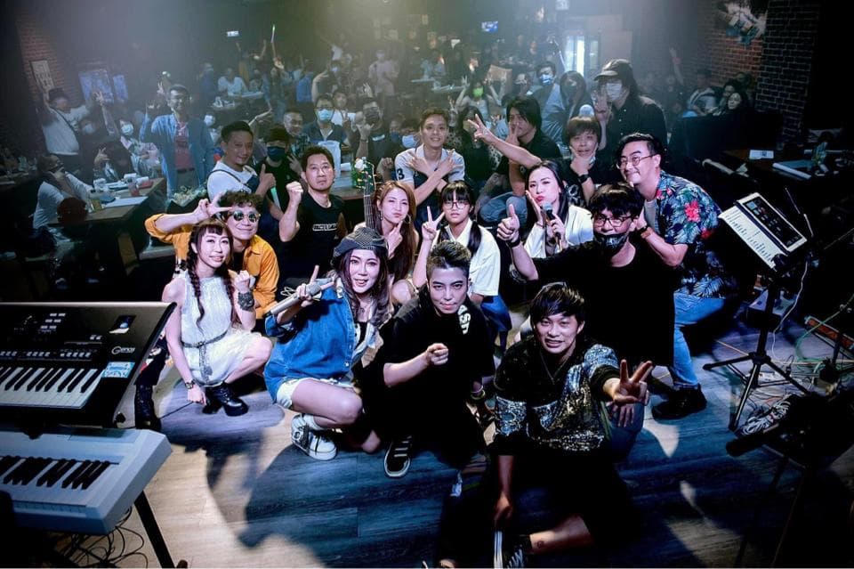 這張「一群朋友聚會唱歌」的照片是一個充滿歡樂的場景,照片裡有許多朋友圍坐在音樂器材旁唱歌。