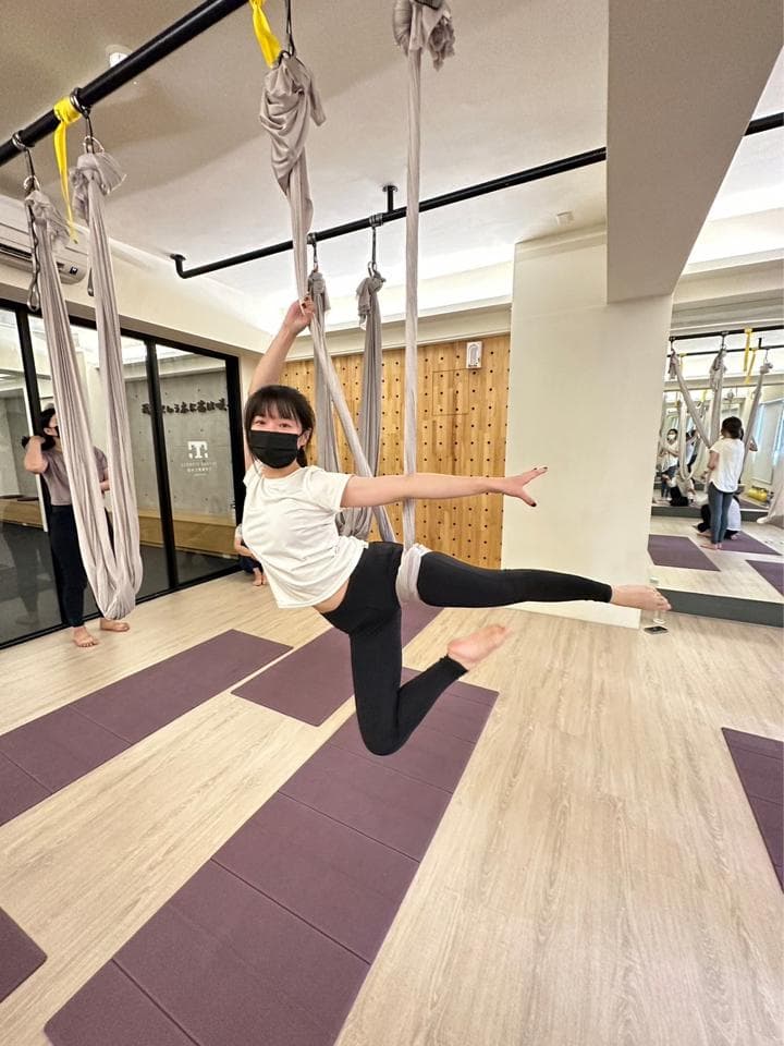這張照片是關於空中瑜珈的。空中瑜珈可以幫助你提升核心力量、柔軟度和平衡感,同時也能舒緩壓力。想要學習空中瑜珈嗎?快到PRO360找教練吧!