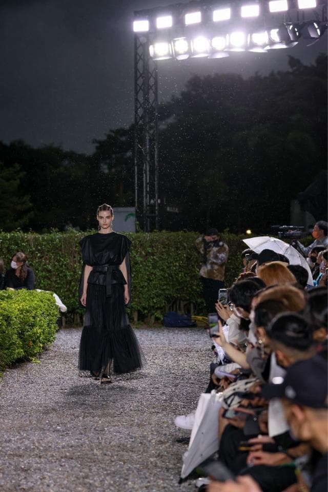 這張「時尚走秀」的照片是一個穿著黑色洋裝的模特兒在雨中走秀,背景是一群觀眾。