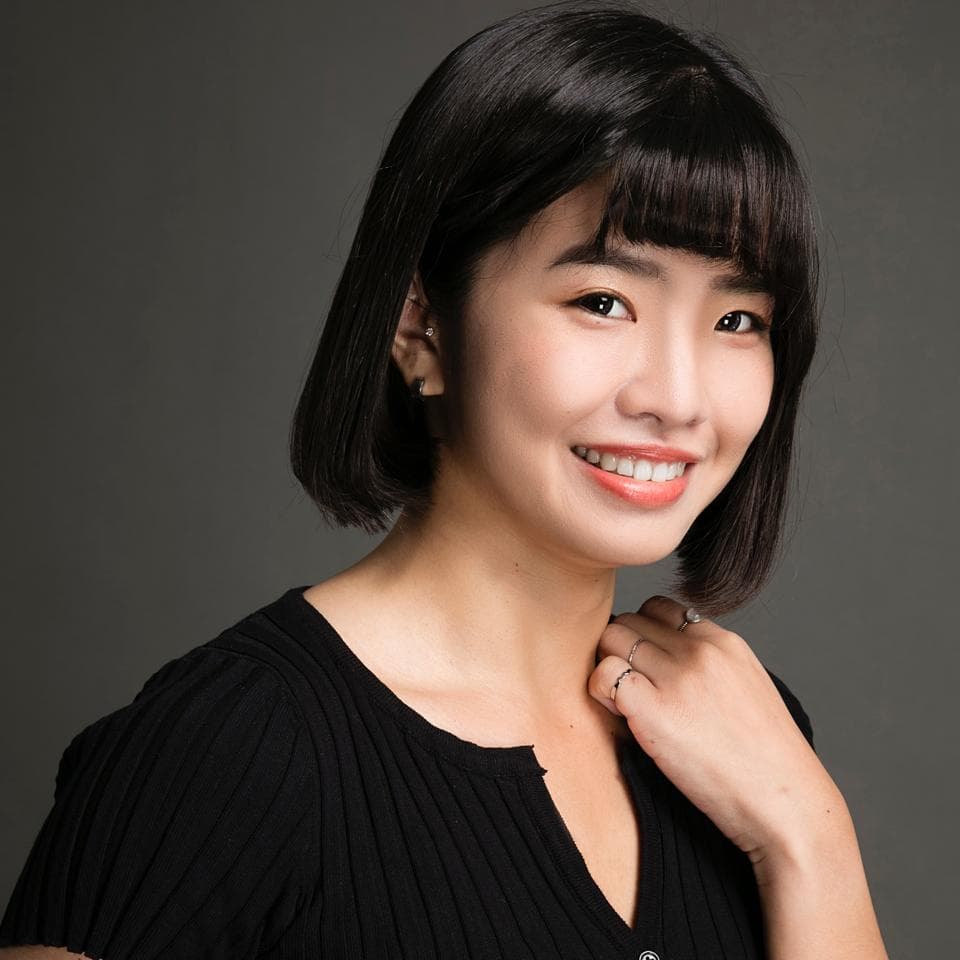 這張照片是一個年輕女性的肖像照,她身穿黑色上衣,笑容燦爛,眼神充滿自信。她短髮微卷,髮型時尚,襯托出她甜美的五官和明亮的眼神。