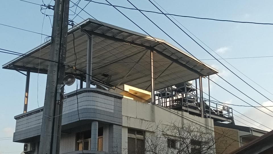 1) 照片顯示一棟建築物,建築物屋頂上有個金屬棚架,棚架下方有電線桿
