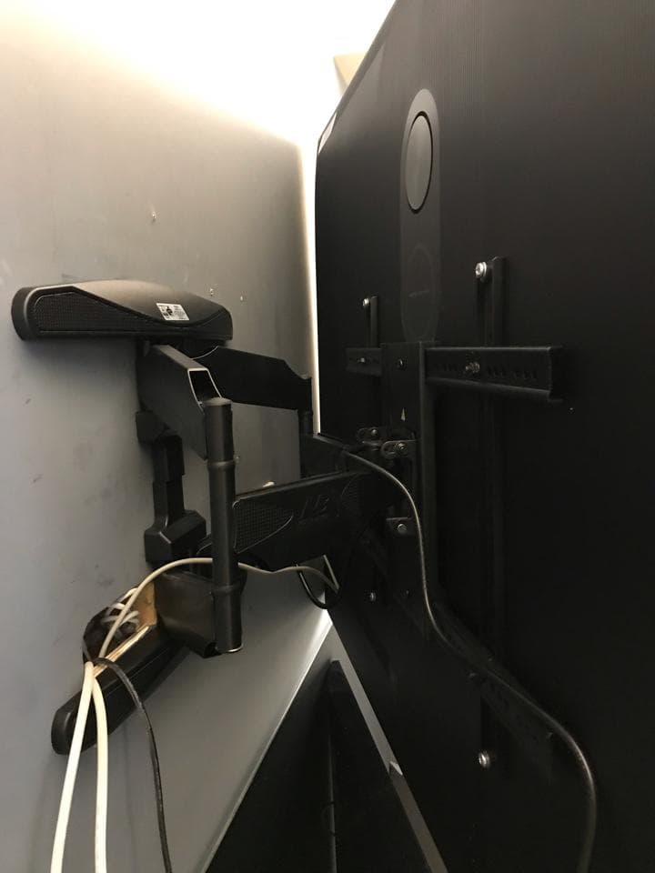 這張照片是一台電視牆壁安裝的畫面,電視用一個黑色的支架固定在牆上,支架上有許多黑色的線路,電視是黑色的。