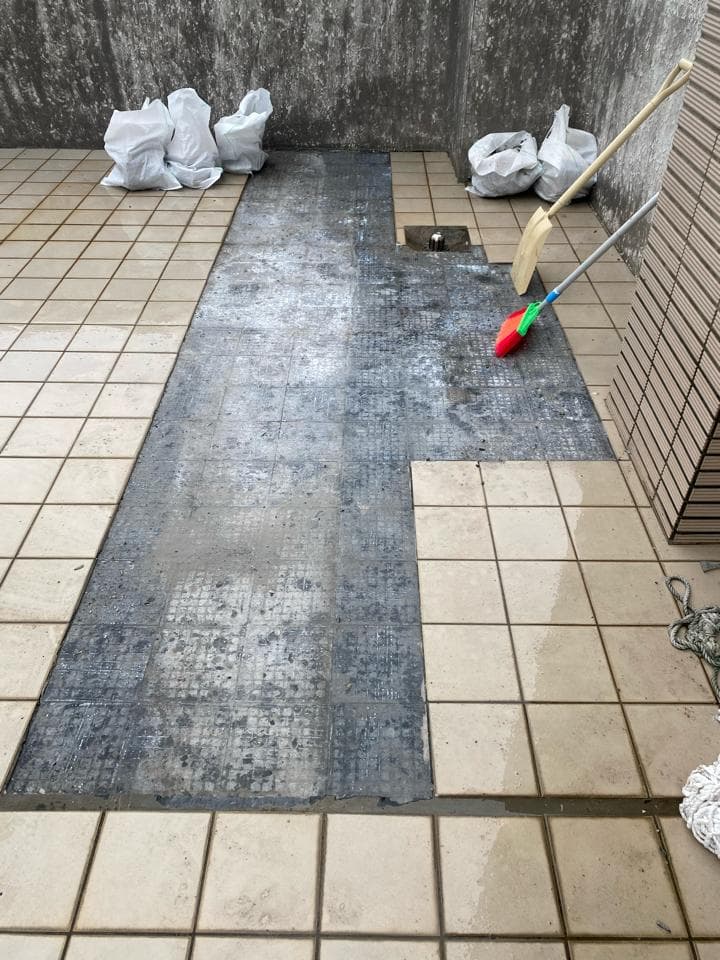 1) 照片顯示一個水泥地板上有一個新的防水層,地板上放著一些白色塑膠袋和兩把掃帚
