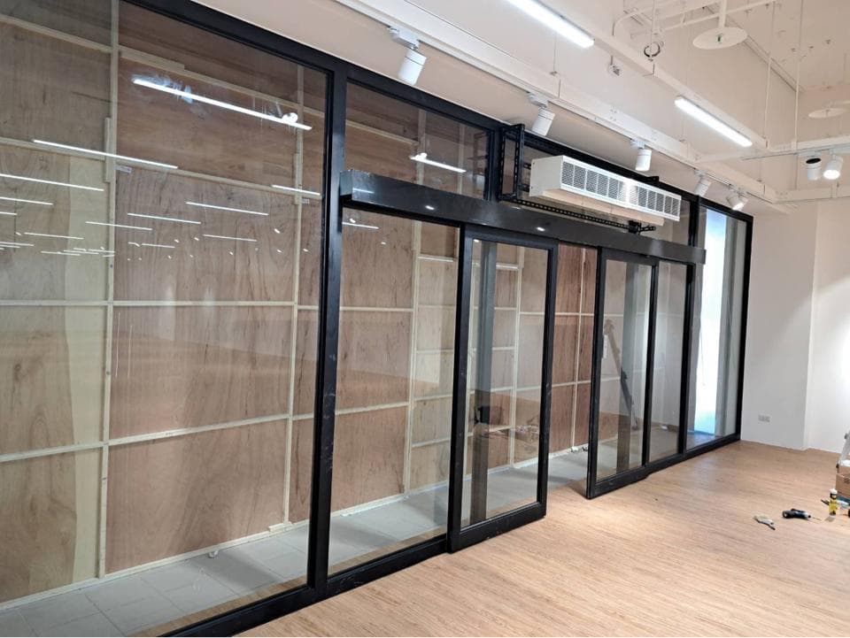 1) 照片顯示一個由黑色框架和玻璃組成的門,門後是一個空的房間,牆壁是木頭,地板是木頭