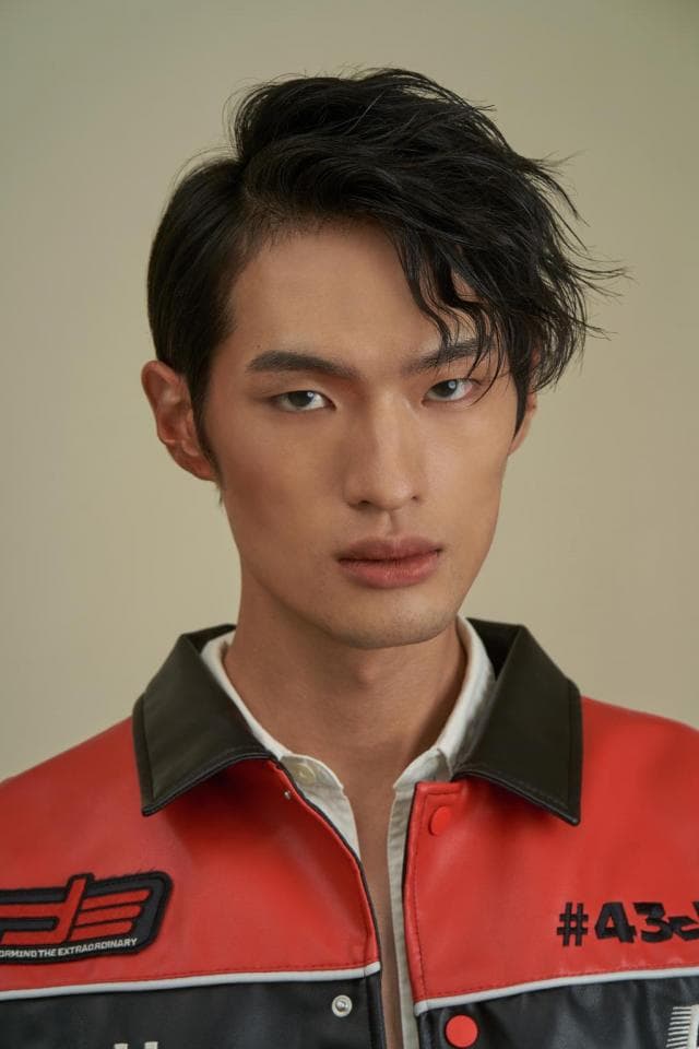 這張照片是一個穿著紅色和黑色夾克的年輕人。他有一頭黑色的頭髮,穿著白色的襯衫。最顯眼的是他夾克上的紅色和黑色設計,看起來像是賽車服。