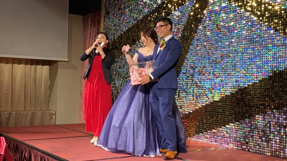 這張婚禮的照片是一個新郎新娘站在舞臺上,新娘穿著一件藍色的禮服,新郎穿著一套藍色的西裝,他們正在接受朋友的祝福。