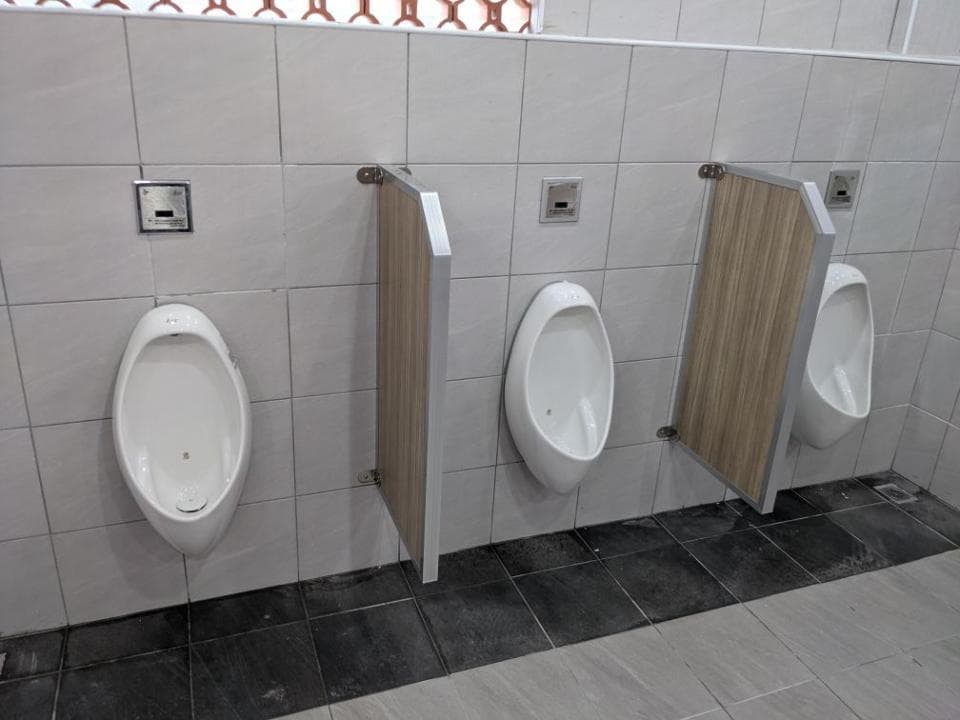 1) 這張照片顯示了三個白色瓷磚 urinal,它們位於一間公共廁所中,每個 urinal 都裝在牆上的單獨隔間中