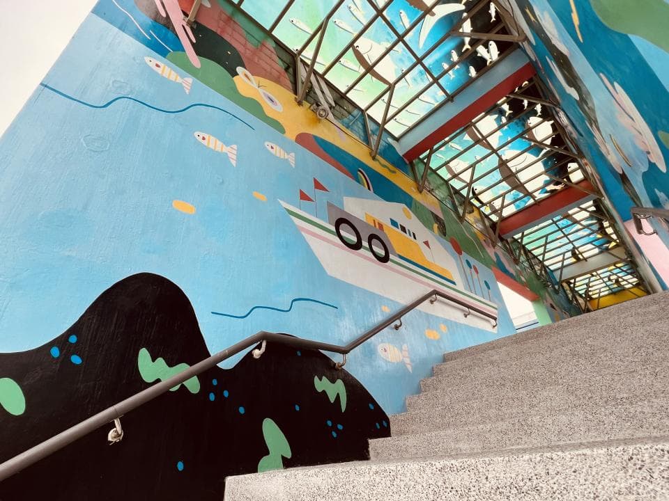 這張「塗鴉牆與樓梯」的照片是 一個充滿童趣的公共空間,牆上繪製著海洋生物和船隻,樓梯則是用白色石材打造,整體感覺清新明亮。
