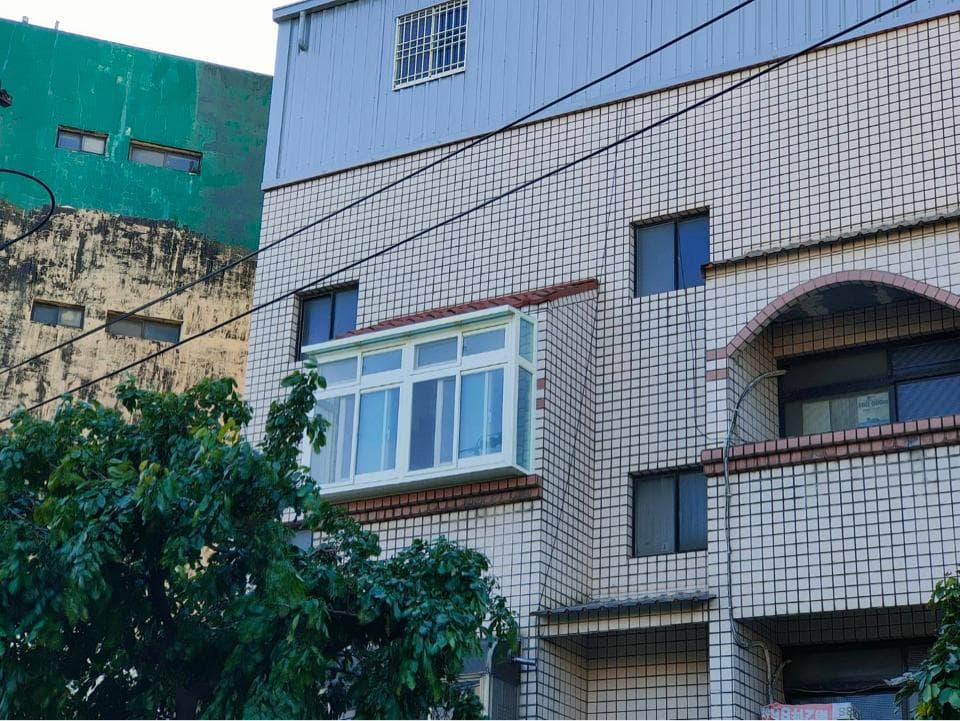 這張照片是 一棟有著白色磚牆的建築,建築物有兩個大大的窗户,其中一個有着白色的窗框,另一個是黑色的窗框。