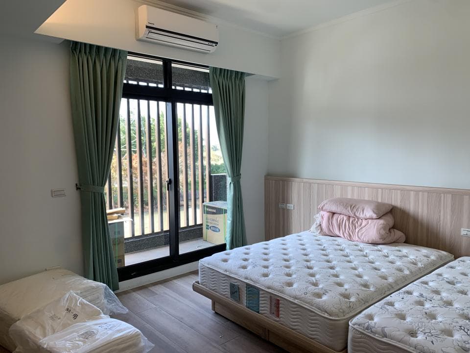 1) 照片顯示一個臥室,房間裡有一張雙人床和一張單人床,房間的色調以淺色系為主,房間裡有一個落地窗,窗戶外可以看到樹木