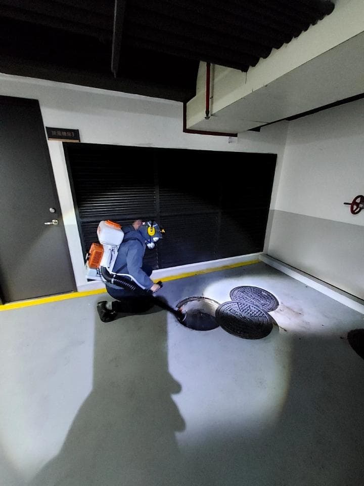 1. 照片顯示一名身穿橙色背心和藍色褲子的男子,手持工具,彎腰看著地面上的兩個黑色圓形排水孔