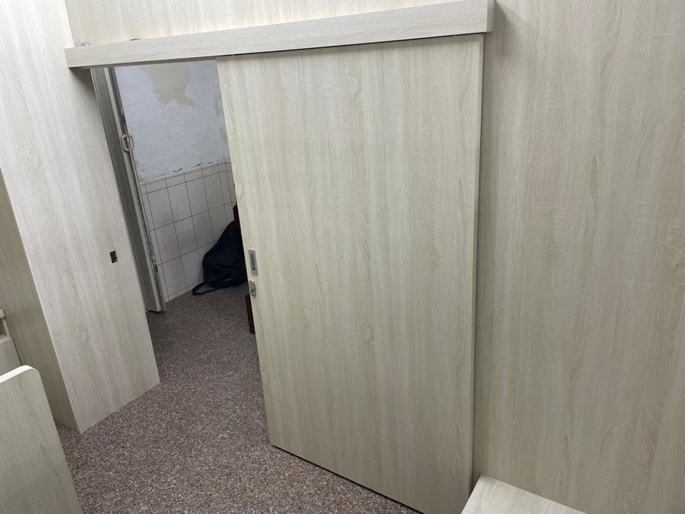 這張照片是一個房間的門,門是木紋的,顏色是淺棕色,門把手是銀色的,門是滑動式的。