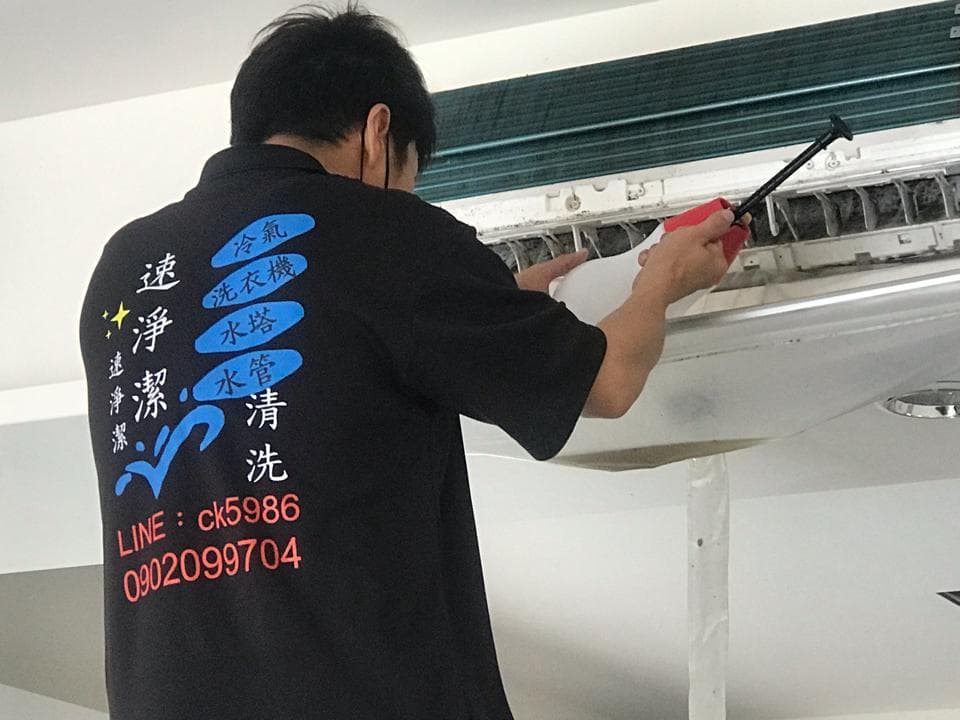 這張照片是一個穿着黑色T恤,上面印着藍色字體,寫着「通/冷氣/水/清洗/洗」的男子,他正在修理冷氣。