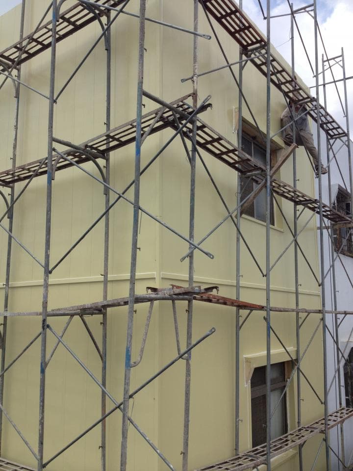 1) 照片顯示一棟建築物正在進行施工,建築物的外牆上搭設了鷹架,鷹架上有一些工作人員,建築物周圍的環境看起來像是工地