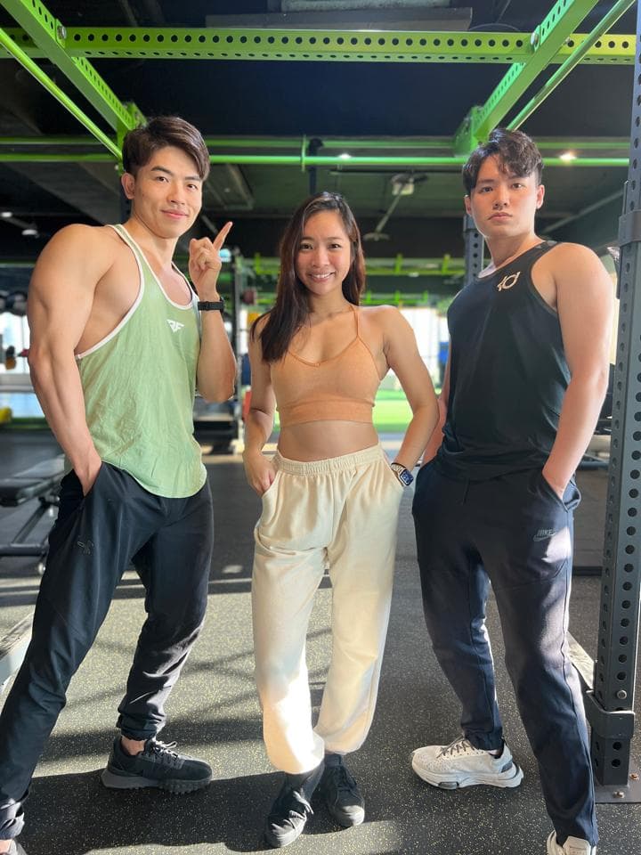 這張「健身房」的照片是三個朋友,兩個男生和一個女生,他們穿著運動服在健身房裡。其中一個男生指著鏡頭,另一個男生則站在他旁邊,而女生站在中間。
