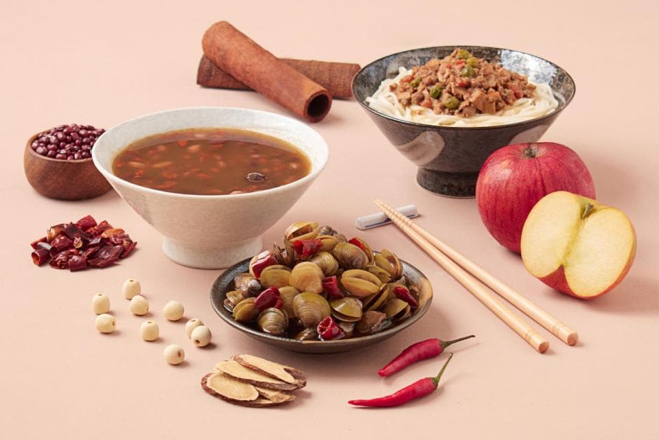 這張「食物」的照片是一碗紅豆湯、一碗拌麵、一盤醃製的貝類、兩個蘋果、一些辣椒、一些蓮子、一些薑片和一些肉桂棒。