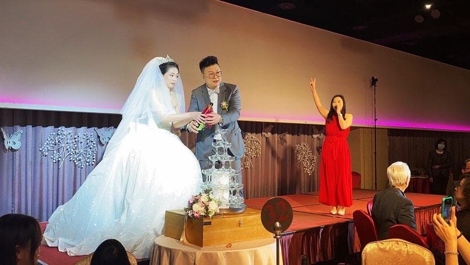 這張婚禮的照片是一對新人正在進行香檳塔儀式,新娘穿著白色婚紗,新郎穿著西裝,他們正在一起倒香檳。