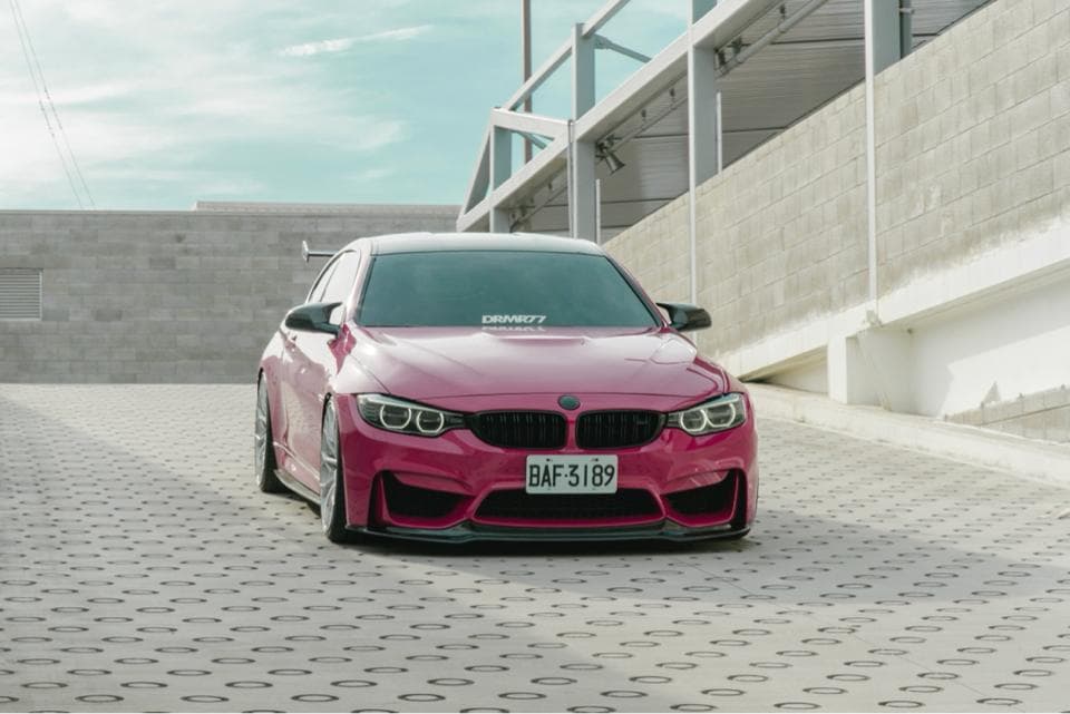 這張照片是一輛粉紅色的寶馬M4,它停放在水泥地上,周圍是建築物。車子看起來很新,很漂亮。