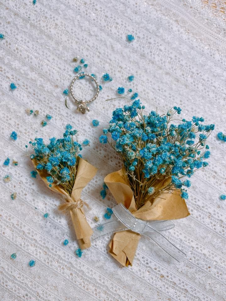 1) 照片中有一張白色蕾絲桌布,上面放著兩個用牛皮紙包裝的小藍色花束,和一個銀色戒指