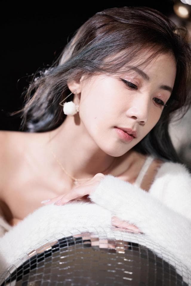 這張照片是一個女孩靠在鏡球上,她穿著一件白色毛衣,她的手輕輕地放在鏡球上,她的表情看起來很溫柔。