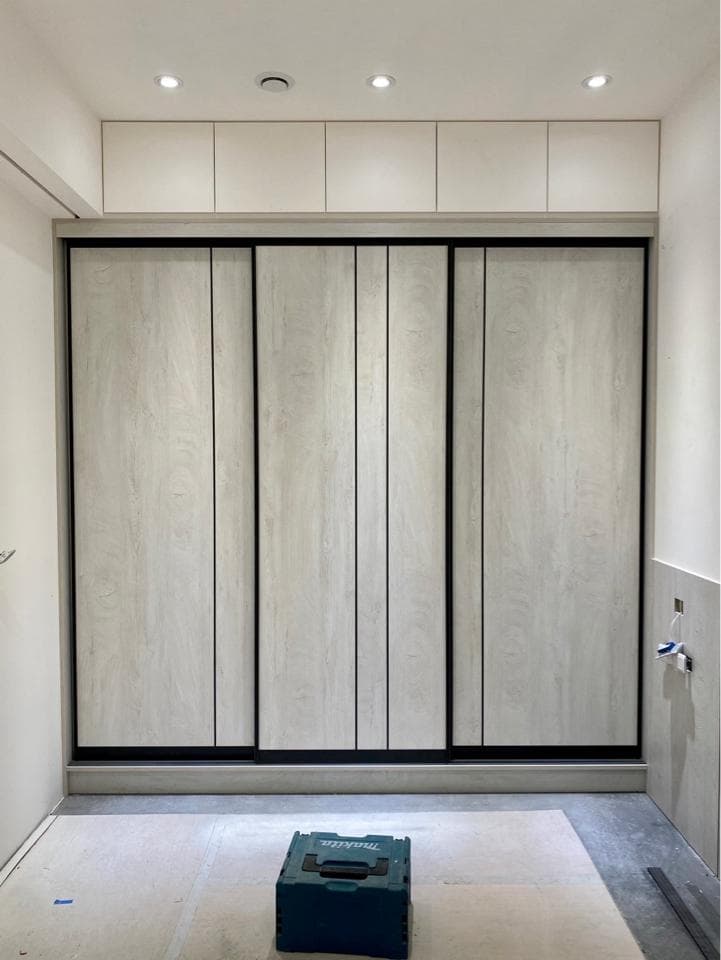 這張照片是一個現代化的衣櫃,它有三個滑門,每扇門上都有細緻的木紋,並且以黑色邊框裝飾,散發出簡約而優雅的風格。