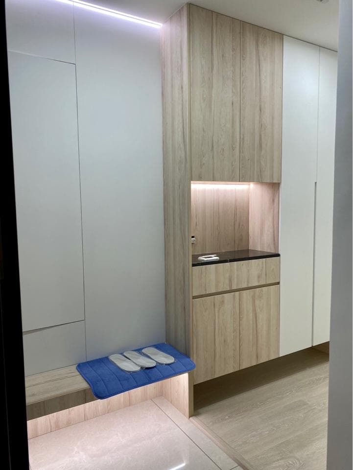 這張照片是一個現代化的玄關,最重要的是一個木質的鞋櫃和一個藍色的地毯,地毯上放著三雙白色的拖鞋。