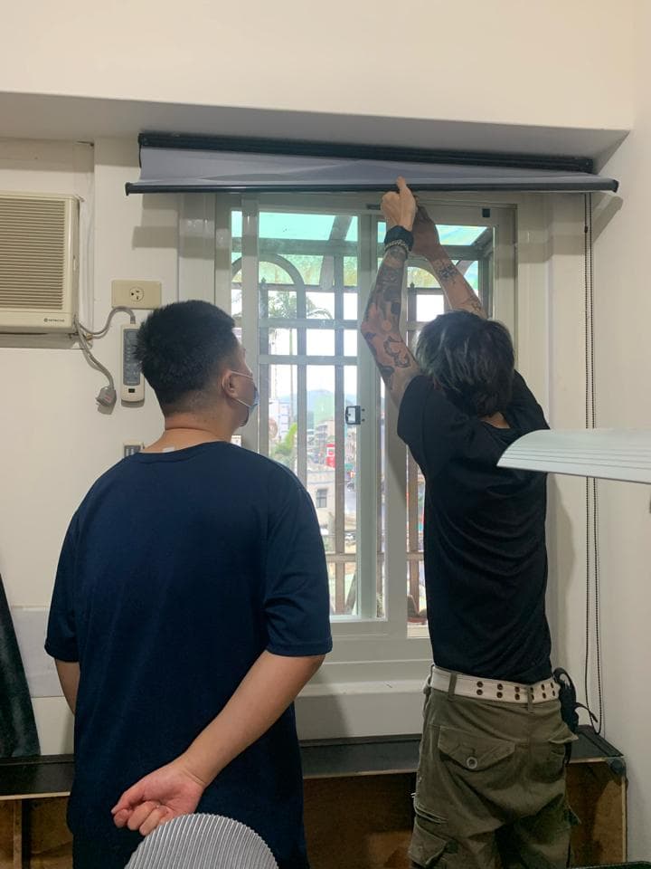 照片中,兩個男人站在窗戶前,其中一個男人正在安裝窗簾,另一個男人站在旁邊觀看