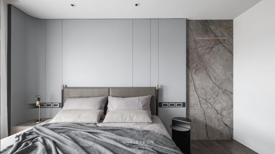 這張「臥室」的照片是一張大床,床頭板是灰色的,床單是灰色的,牆壁是白色的,有一面牆是灰色的石頭牆。