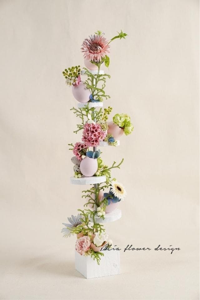 1) 照片顯示一個白色花架,上面擺放著各種粉色、藍色和黃色的花朵和裝飾性雞蛋