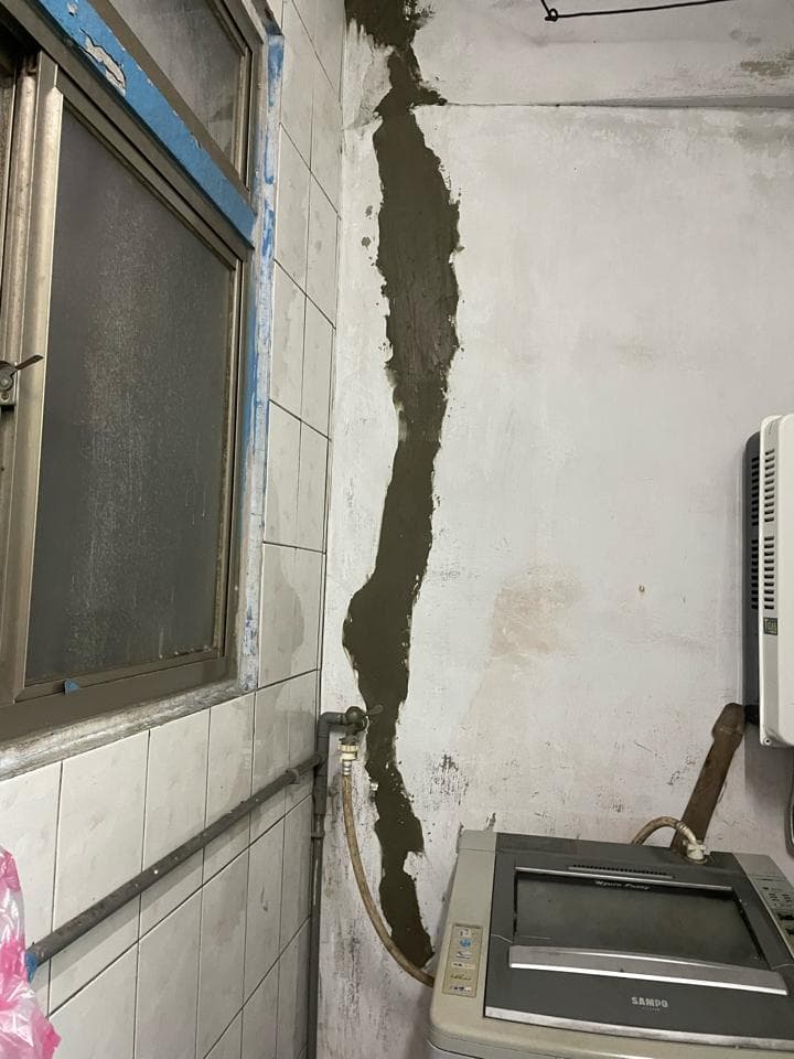 1) 照片顯示一間浴室,牆上有一個大裂縫,已經用水泥填補,旁邊放著一台洗衣機