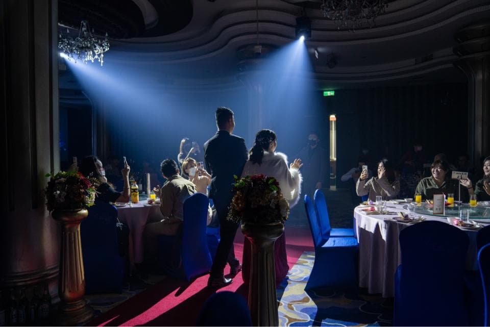 這張婚禮的照片是一對新人在聚光燈下擁抱,賓客在旁邊歡笑鼓掌,場面溫馨感人。
