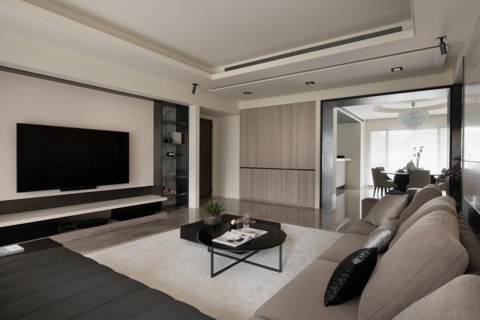 這張客廳的照片是一間現代化的客廳,佈置簡潔,以灰色和白色為主色調,傢俱以淺色系為主,牆上掛著一臺液晶電視,並設有簡約的電視櫃,整體給人一種舒適寧靜的感覺。