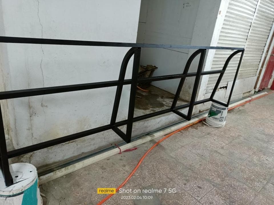 1) 照片顯示一個黑色金屬架子,架子有三個層架,架子安裝在牆壁上,牆壁旁邊有一個橘色的管子