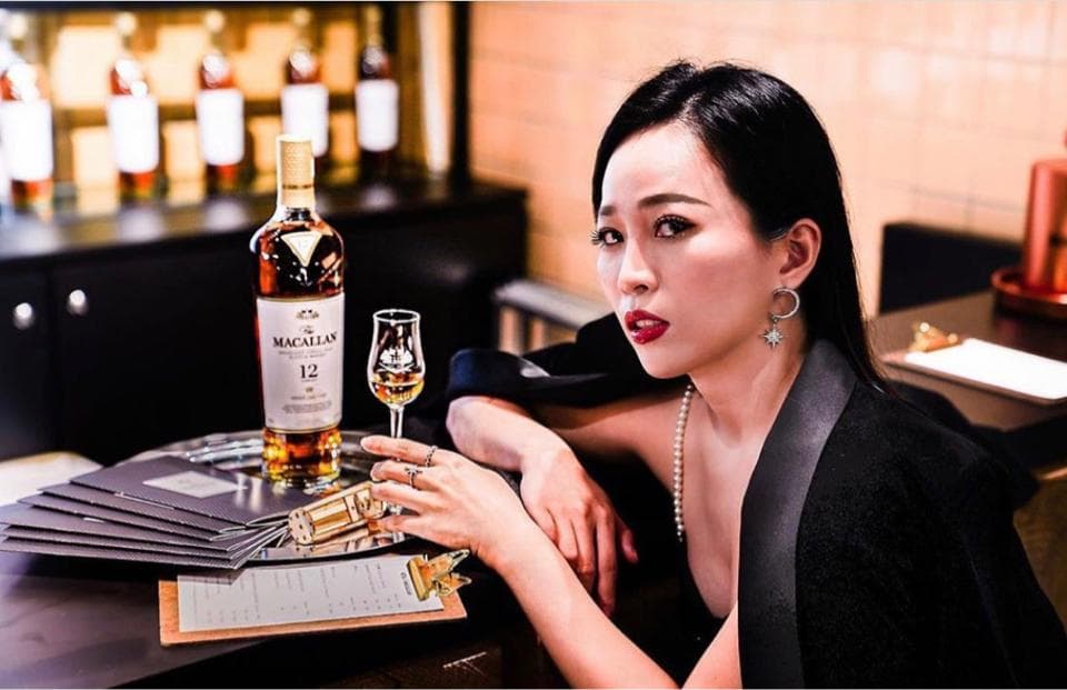 這張照片是一位年輕女性,她穿著黑色的西裝外套,手裡拿著一杯威士忌。