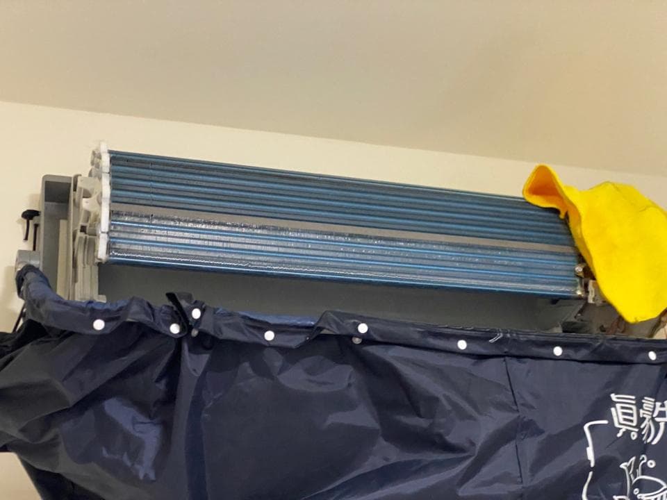 1) 照片中是一台冷氣機的室外機,上面覆蓋著一塊黑色的防水布,冷氣機下方則放置了一個黃色的布