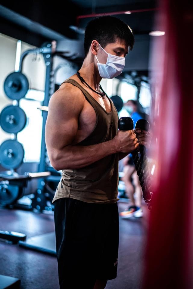 這張照片是一個戴著口罩的男子在健身房舉啞鈴。