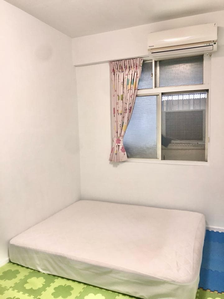 這張照片是一間簡約的房間,房間裡有一張床和一個窗戶,床鋪上鋪著白色的床單,窗戶上有粉紅色的窗簾。