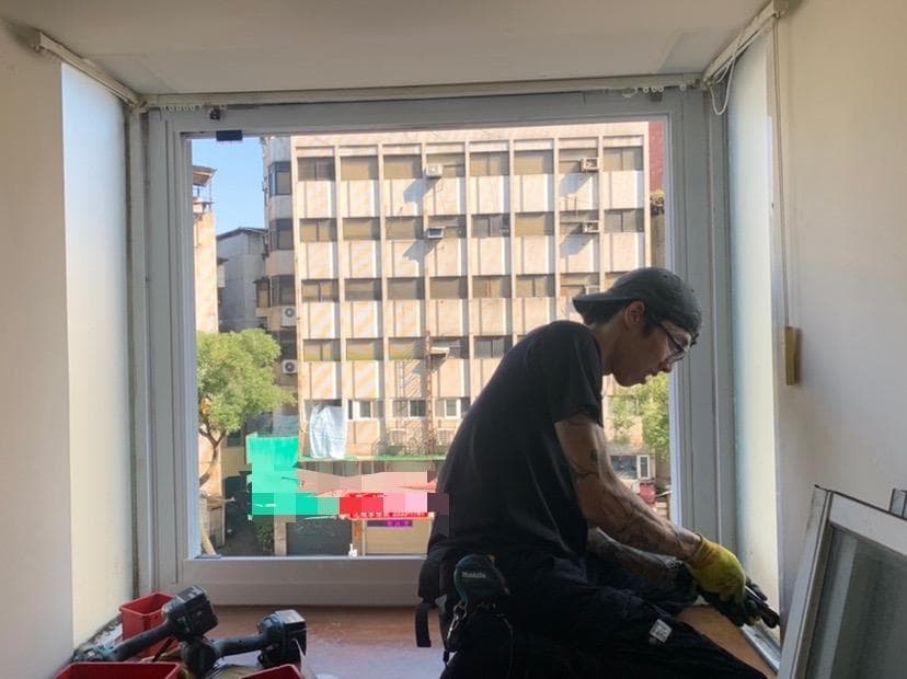 1) 照片中,一個戴著帽子、穿著黑色上衣和長褲的男子正在窗戶旁工作