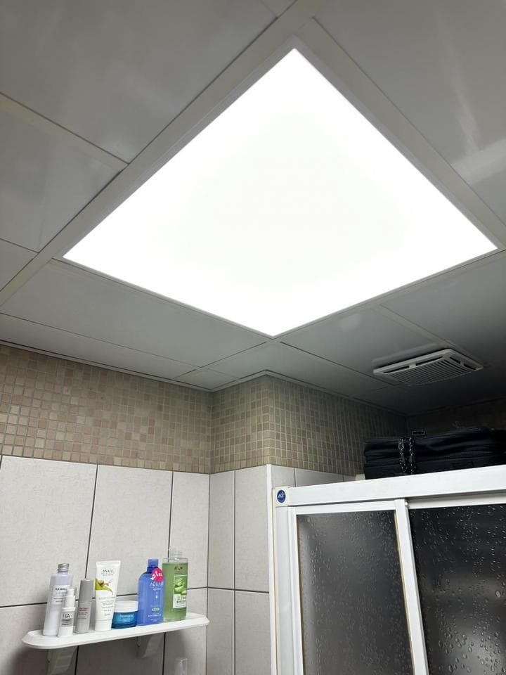 1) 照片顯示一個浴室的天花板,天花板上有個方形的燈,旁邊的牆壁上裝飾著瓷磚,浴室裡有一個淋浴間,淋浴間裡有一個玻璃門,在淋浴間旁邊的架子上放著一些瓶子