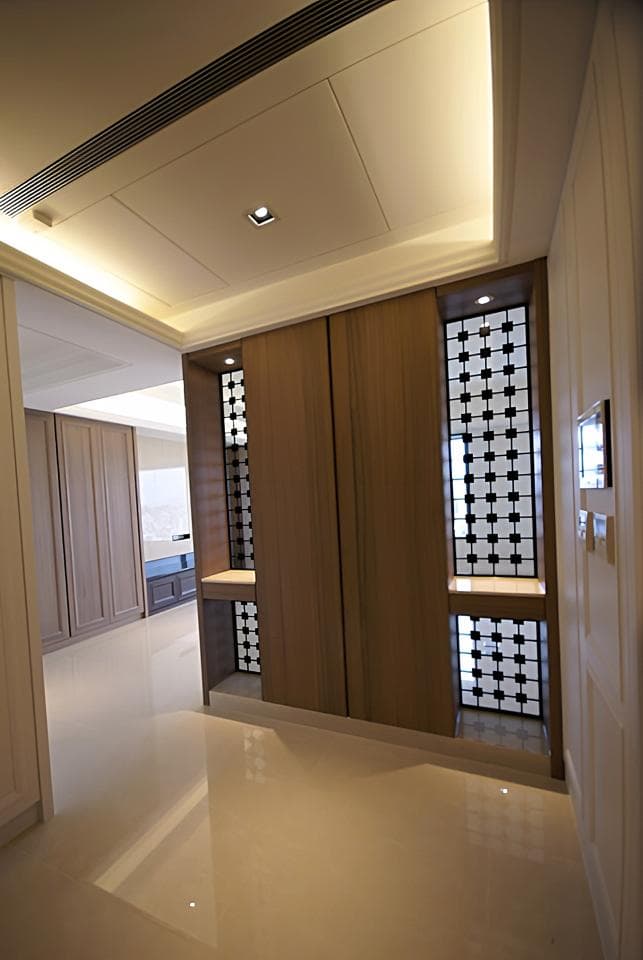 這張照片是一間裝潢精緻的住宅大廳,最顯眼的地方是牆面上方鑲嵌著的格柵裝飾,格柵採用深色木框搭配白色玻璃,呈現出簡約的現代風格,與整體空間的明亮色調形成鮮明對比。