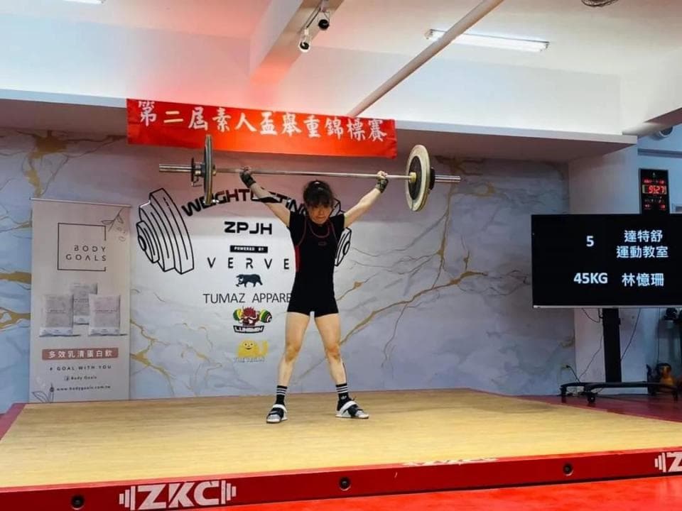 這張照片是一名女性運動員正在舉重。她正在進行舉重比賽,並成功舉起了一個重物。她的動作看起來很標準,顯示出她強壯的體力和出色的技術。