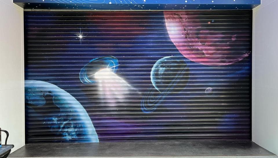 這張照片是一個塗鴉的捲閘門,上面繪製了外太空的景象,其中最顯眼的是一顆紅色的星球,它位於畫面右上角,佔據了相當大的面積,並帶有深邃的宇宙背景。