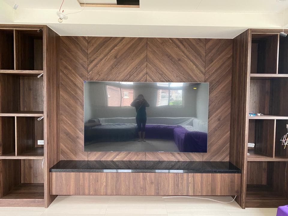 1) 照片顯示一個現代客廳的牆上裝設了一台大型電視機,電視機下有一個木質的電視櫃,兩旁各有一個木質的架子