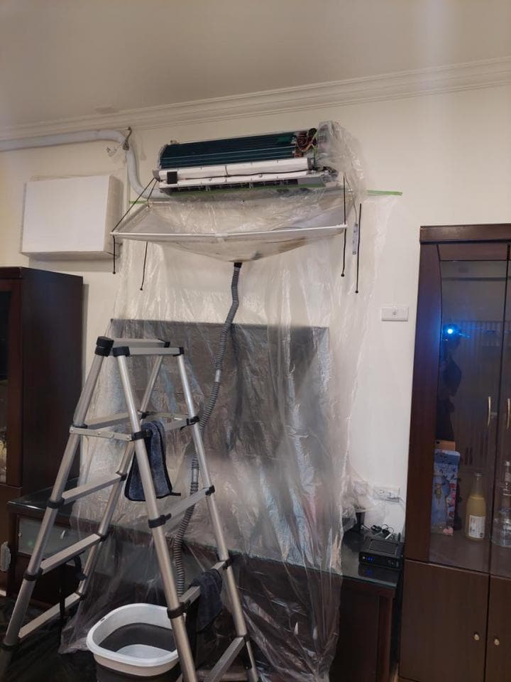 這張照片是一台正在維修中的冷氣,它被一個塑膠布罩住,下方放了一個梯子,還有一個水桶。