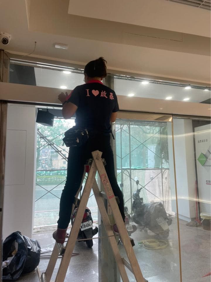 1) 照片顯示一名女子站在梯子上,她身穿黑色T恤,上面印著粉紅色愛心和中文“我愛美食”